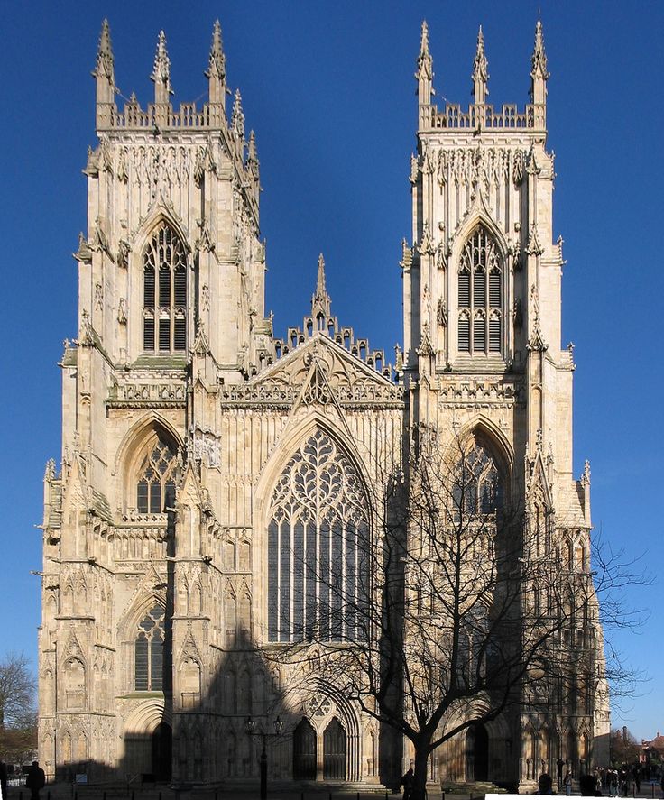 a large cathedral with tall towers and two trees in the foreground, against a blue sky