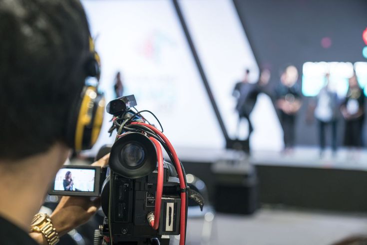 a person with headphones and a video camera taking a photo in front of an audience