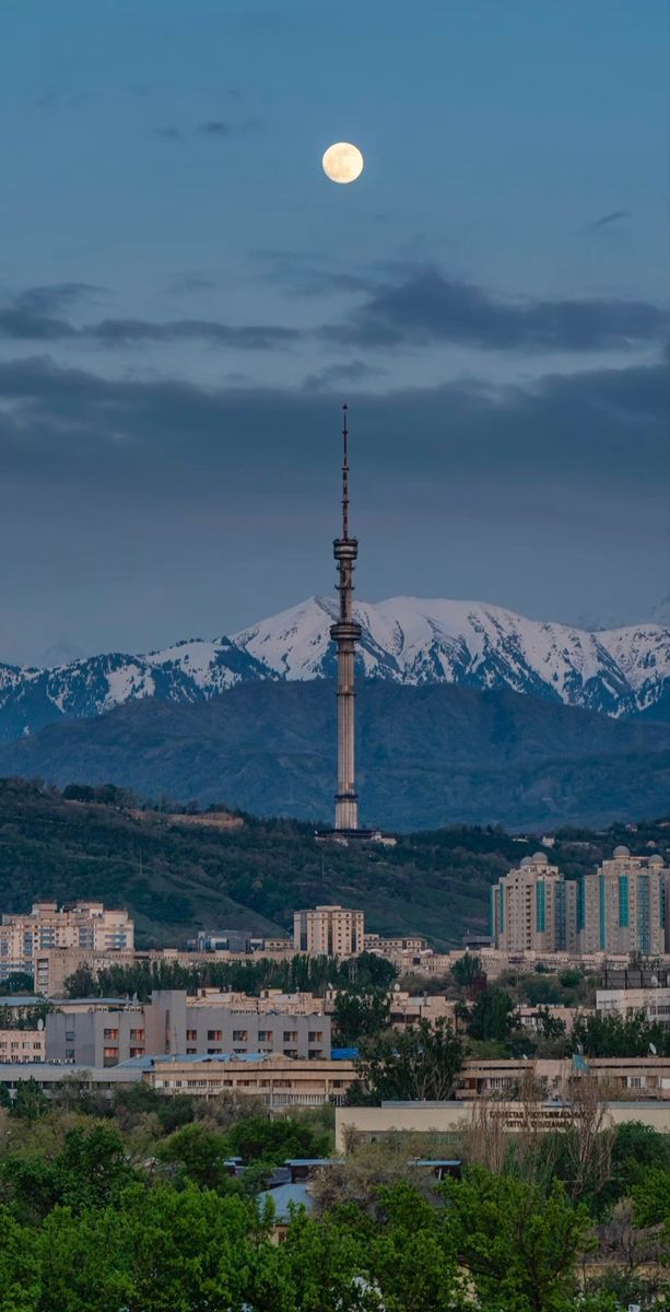 a full moon is seen over a city with snow capped mountains in the back ground