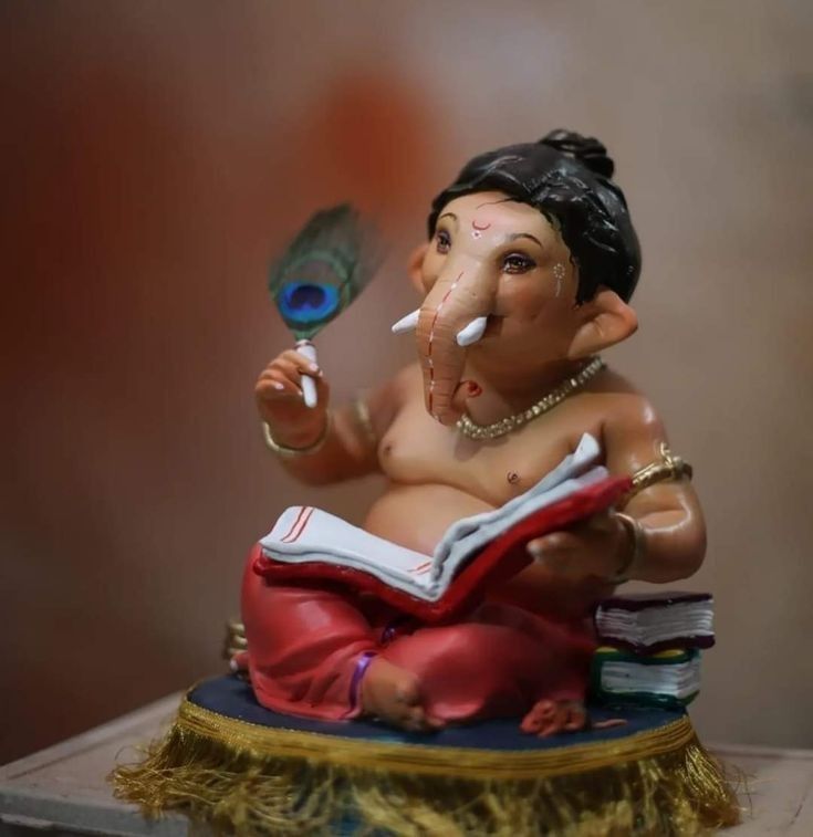 an elephant figurine sitting on top of a pile of books with a feather in it's mouth