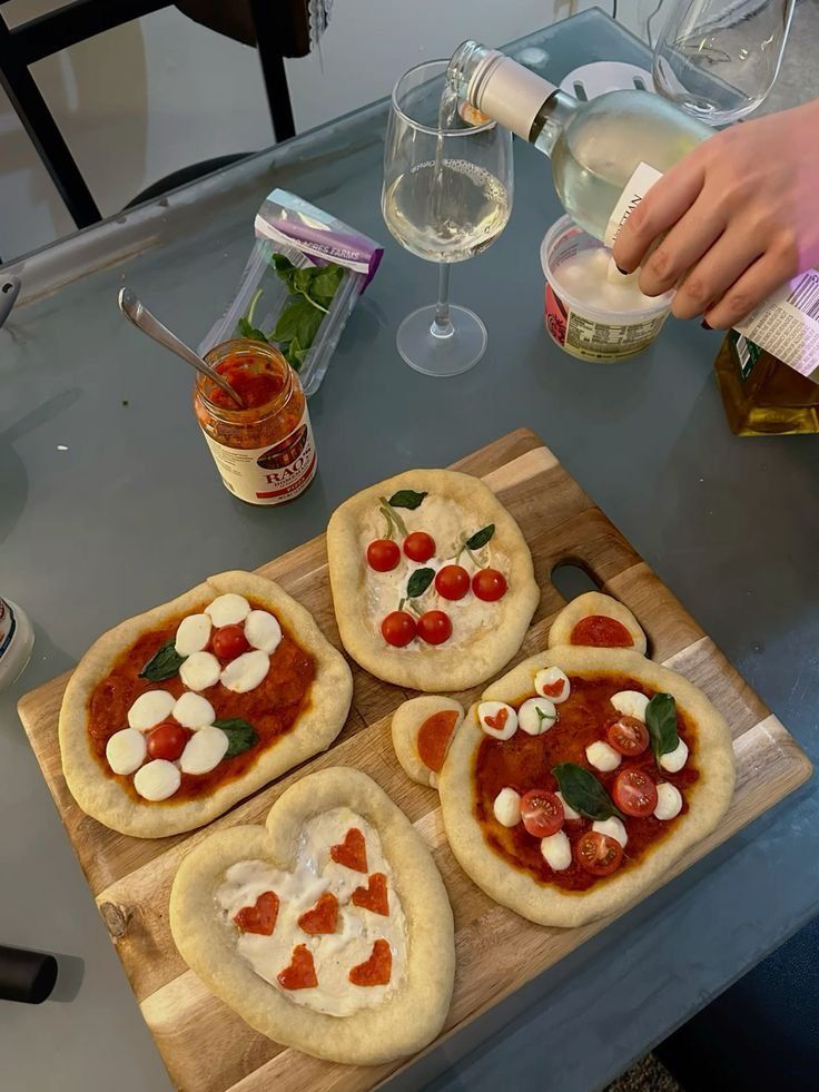 four homemade pizzas with toppings on a cutting board next to bottles of wine