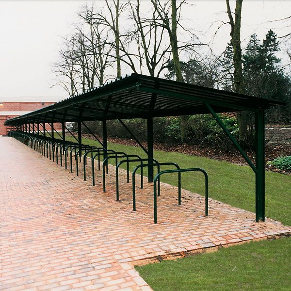 a row of green metal benches sitting on top of a brick walkway next to trees