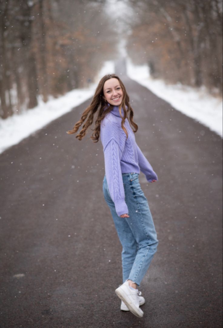 a woman is standing in the middle of an empty road with snow falling on her