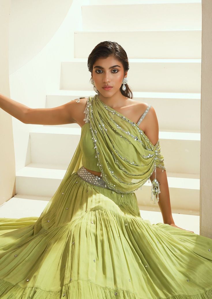 Editor's Note Draped Embellished Choli With An Attached Dupatta With Tassels Paired With A Tiered Skirt With Mirror Sprinkle On It. Fabric: Chiffon, Lining-Satin Color: Green Embroidery Details: Hand Embroidery With Zari, Mirror, Glass Beads And White Beads. Care: Dry Clean Only About the Designer Seema Thukral collection offers glamorous, elegant, and chic clothing for women. It consists of drapes with intricate handwork and embroideries. The brand forte is all about different and unique cuts t Designer Lehnga Unique, Unique Mehendi Outfits, Unique Indian Outfits Style, Unique Gown Design, Unique Dresses Indian, Unique Indian Outfits, Seema Thukral, Draped Lehenga, Indian Bridal Wear Red