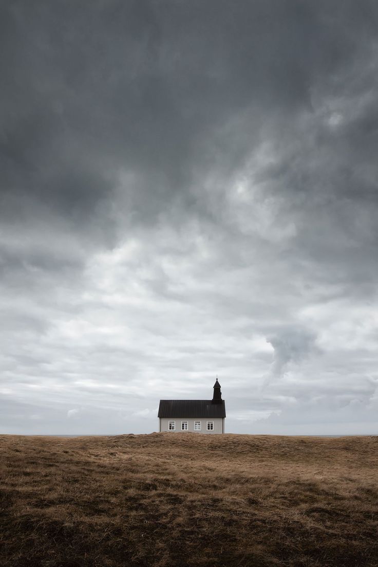 a white house sitting on top of a dry grass field under a cloudy sky with dark clouds