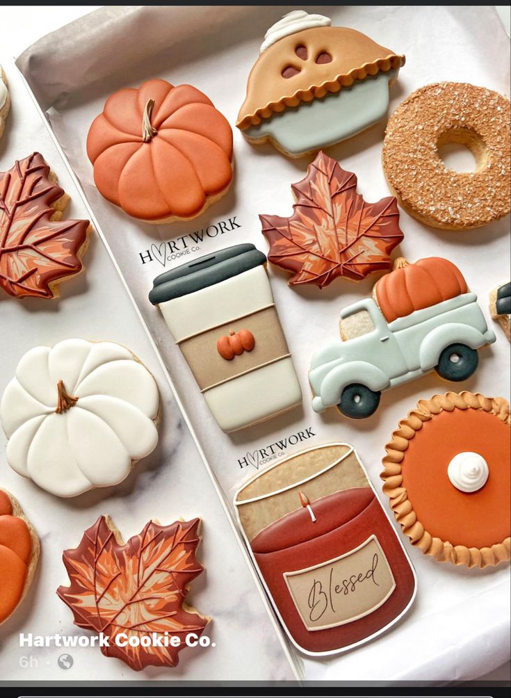 an assortment of decorated cookies and pastries on a white tablecloth with autumn leaves