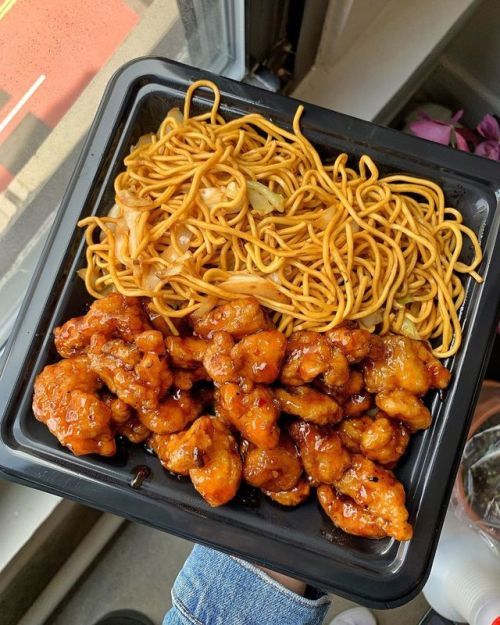 a person holding a tray with noodles and chicken