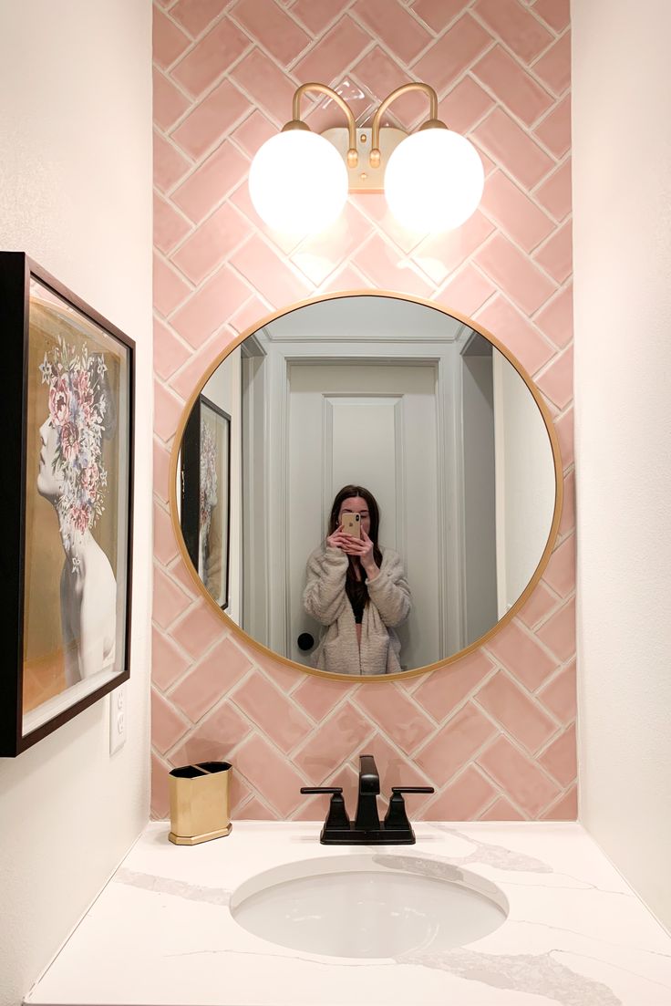 a woman taking a selfie in front of a bathroom mirror with pink tiles on the wall