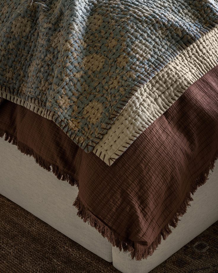 a bed with a brown and blue blanket on it's headboard next to a rug