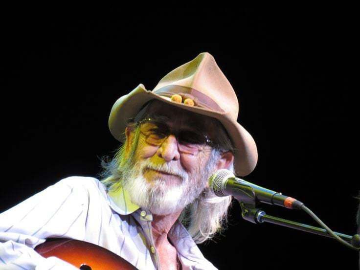 an old man wearing a cowboy hat and holding a guitar in front of a microphone