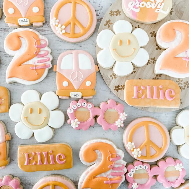 decorated cookies with peace signs and flowers are displayed on a white tablecloth in the shape of numbers