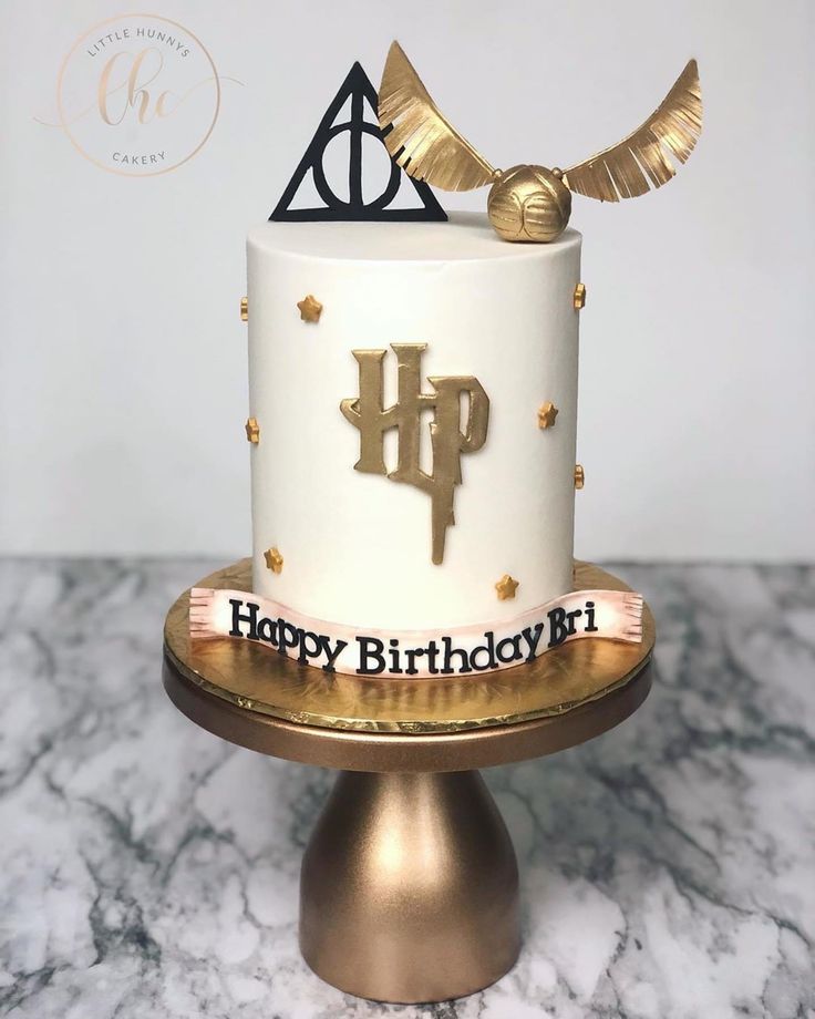 a harry potter birthday cake with gold decorations and an hogwarts symbol on top