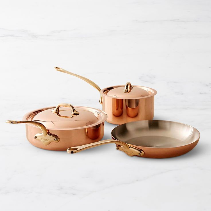 three copper pots and pans on a marble countertop with one holding a gold spoon