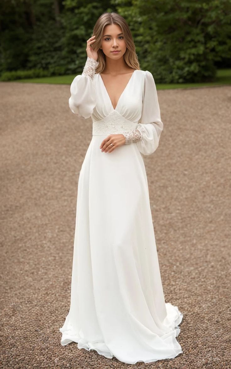 a woman in a white wedding dress standing on gravel road with trees in the background