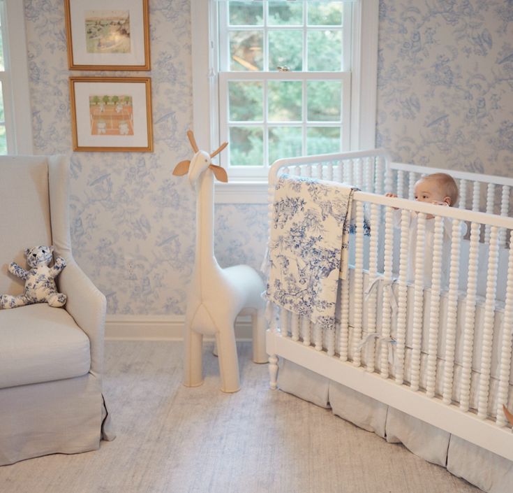 a baby's room with a white crib and blue floral wallpaper on the walls