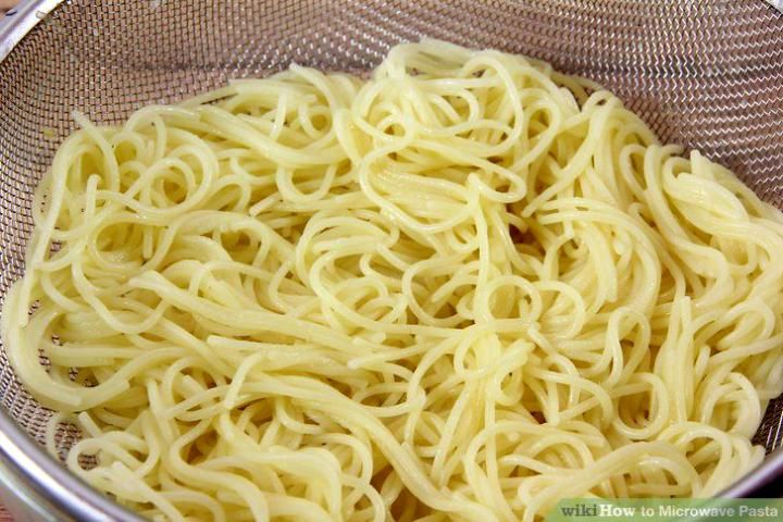 a bowl filled with noodles sitting on top of a wooden table next to a metal strainer