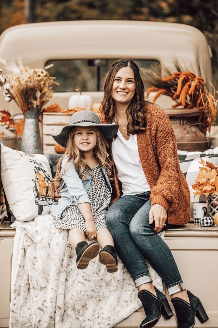 a mother and daughter sitting on the back of a pick up truck with fall decorations