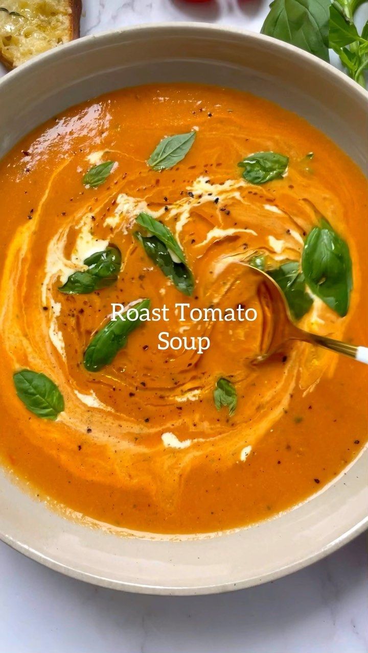 a white bowl filled with tomato soup and garnished with basil leaves on top