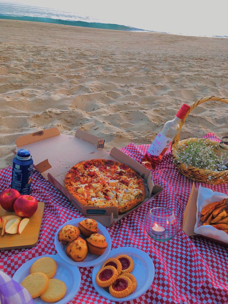 a picnic on the beach with pizza, cookies and fruit is ready to be eaten