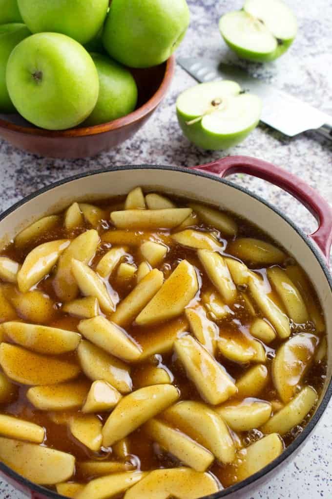 apples and caramel sauce in a red pot on a table next to green apples