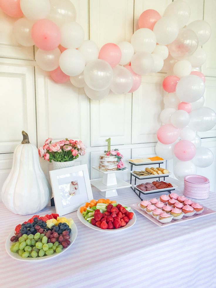 a table topped with plates of fruit and desserts next to a balloon filled wall