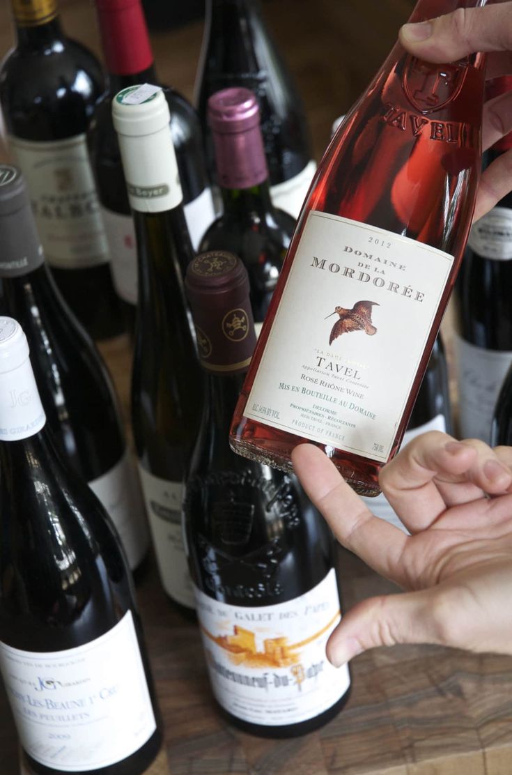 a person holding a bottle of wine in front of several bottles of wine on a table