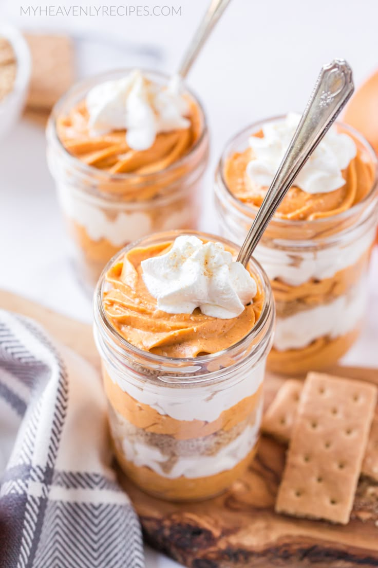 three small jars filled with desserts on top of a wooden cutting board next to crackers