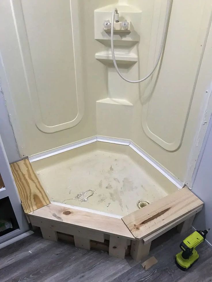 an unfinished shower stall is being installed in a bathroom with wood planks on the floor