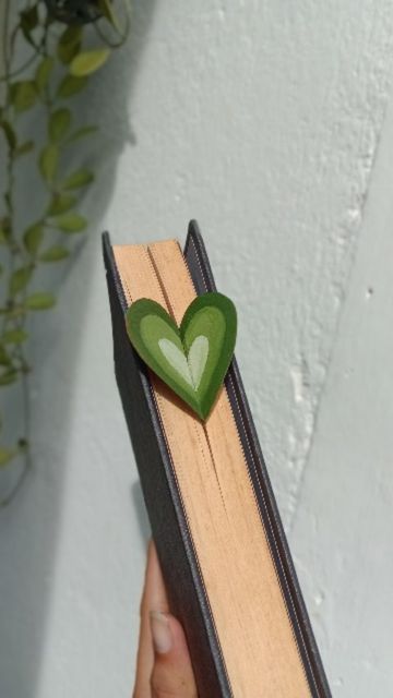 a hand holding a wooden book with a green heart on it