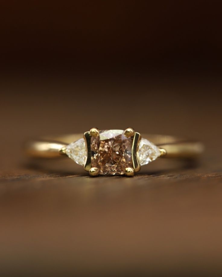 an engagement ring with two pear shaped diamonds on the side, set in yellow gold