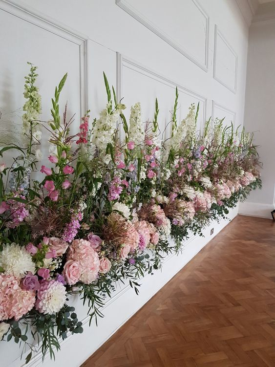 a row of flowers sitting on top of a wooden floor next to a white wall