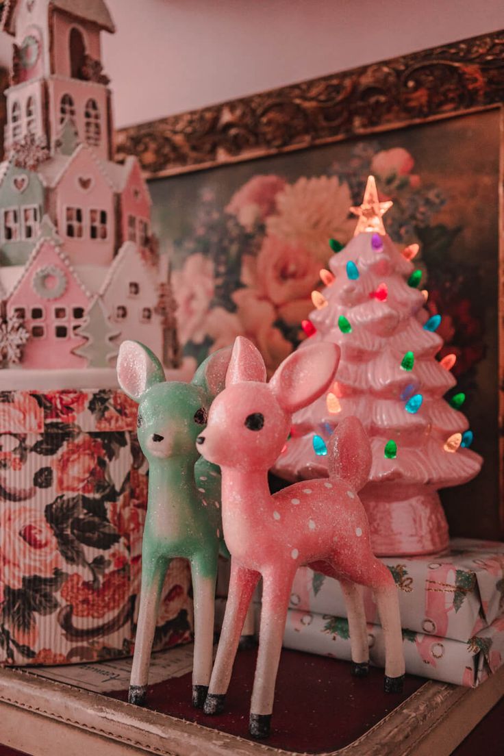 two little deer figurines sitting next to a christmas tree