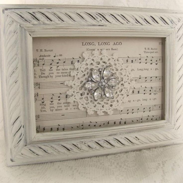 a white frame with music sheets and a flower on the front, sitting on top of a table