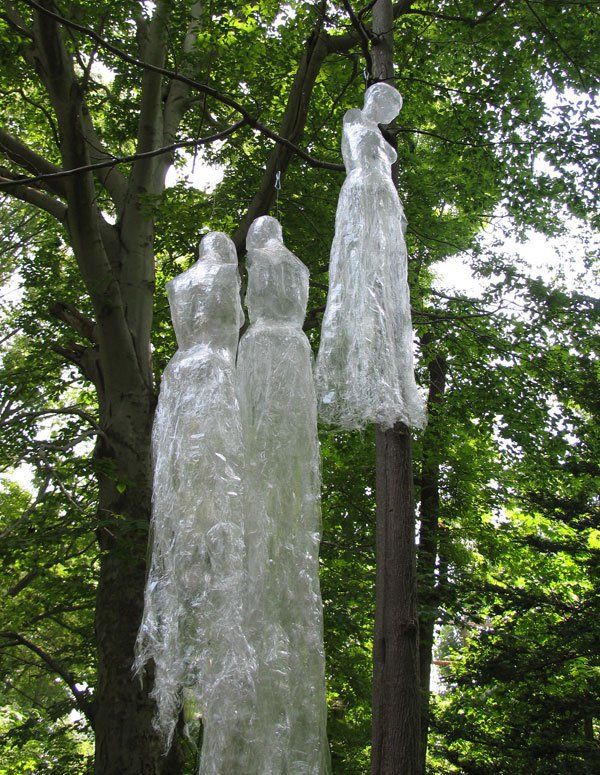 three plastic dresses hanging from a tree in the woods