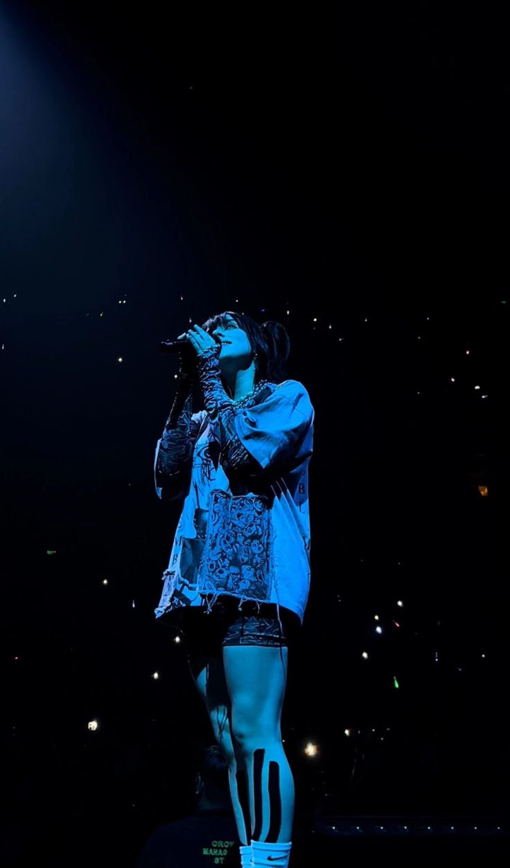 a woman standing on top of a stage with her hands in her mouth while singing into a microphone