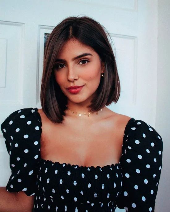 a woman with short hair wearing a black and white polka dot top posing in front of a door