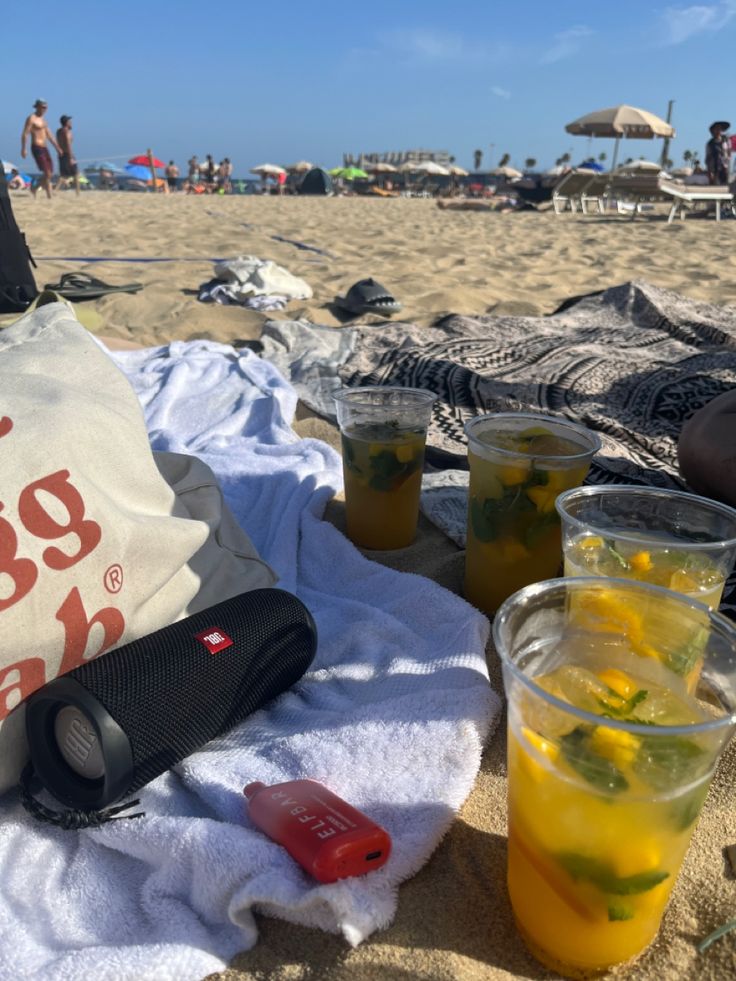 there is a bag and cups on the beach with people in the sand behind it