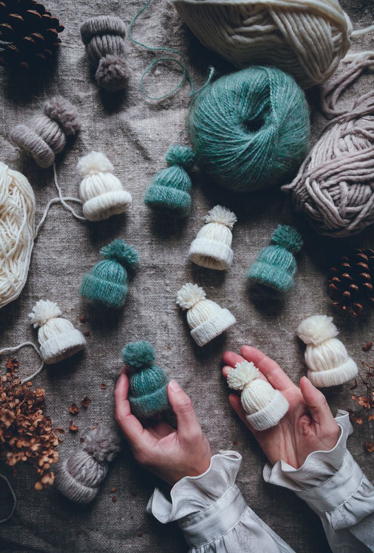 two hands are holding balls of yarn and knitting needles on a table with other crochet items