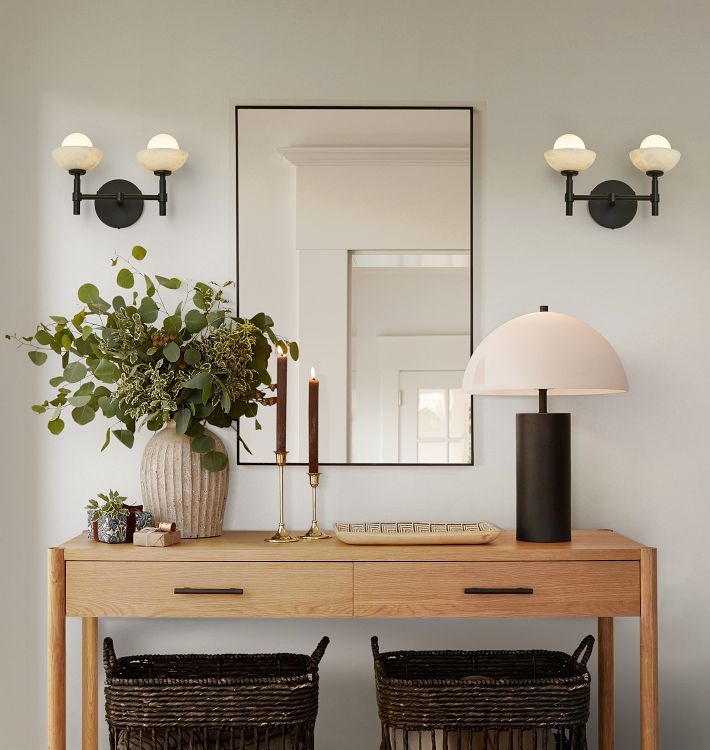 a wooden table topped with two baskets under a mirror next to a lamp and plant