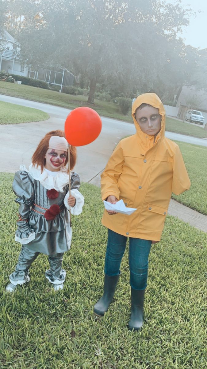 two children dressed up as clowns and one is holding a red balloon in the grass