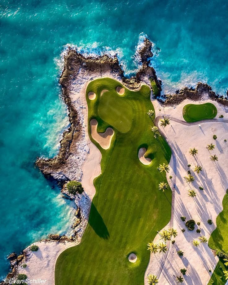 an aerial view of a golf course near the ocean with palm trees and blue water