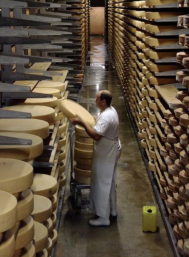 a man standing next to stacks of cheese in a room filled with shelves full of cheese