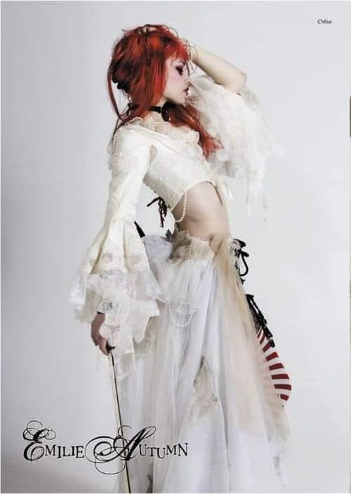 a woman with red hair wearing a white dress and holding a cane in her hand