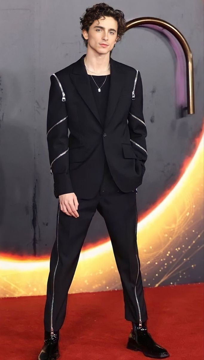 a man in a black suit standing on a red carpet with his hands in his pockets