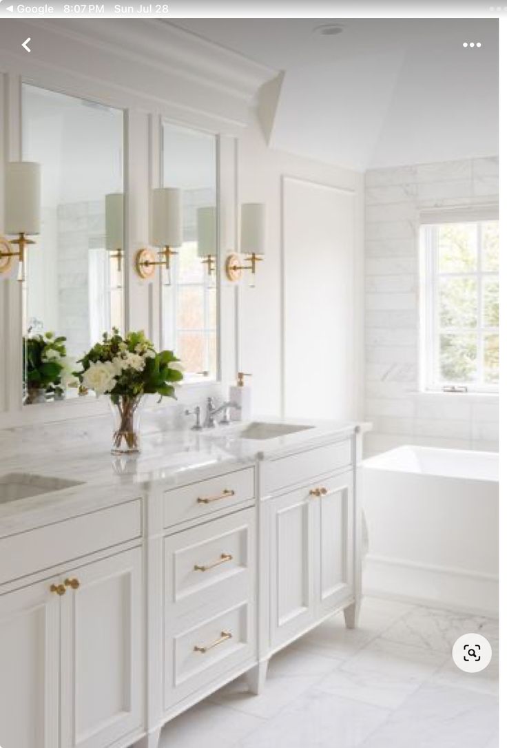 a white bathroom with two sinks and a bathtub next to a large mirror on the wall