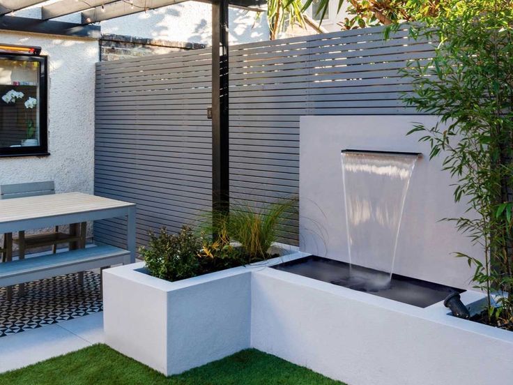 an outdoor fountain in the middle of a small garden area with grass and plants around it