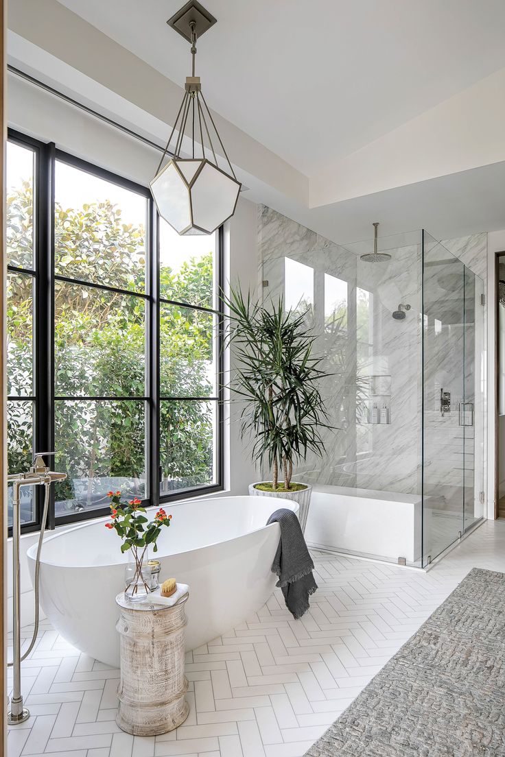 a white bathtub sitting next to a large window in a bathroom under a potted plant