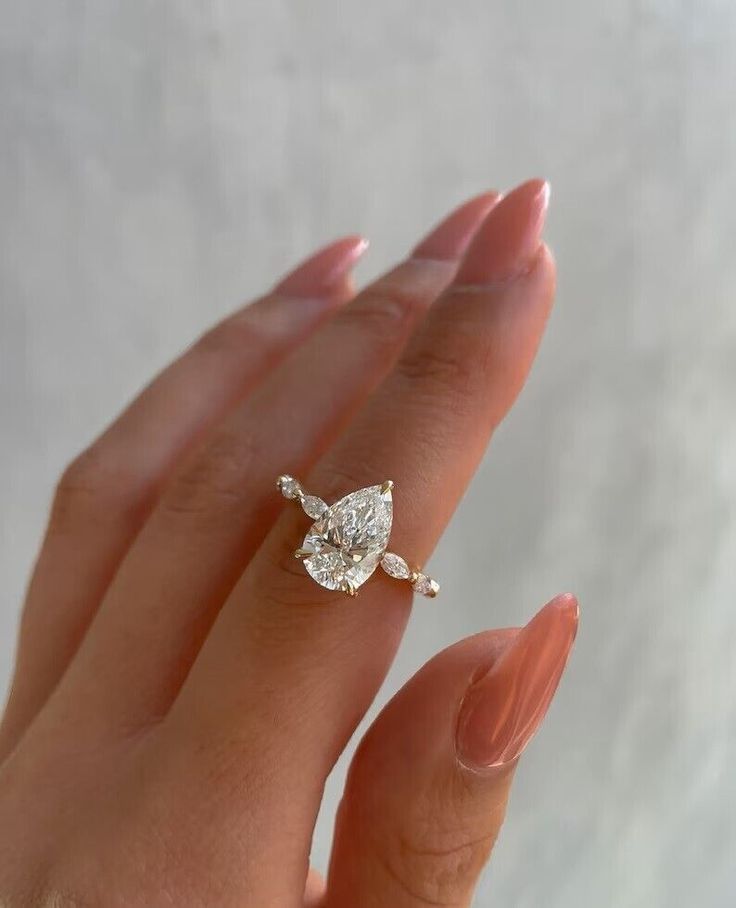 a woman's hand holding an engagement ring with a pear shaped diamond on it