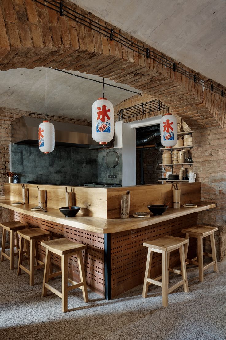 a restaurant with wooden tables and stools in front of the counter area, surrounded by brick walls