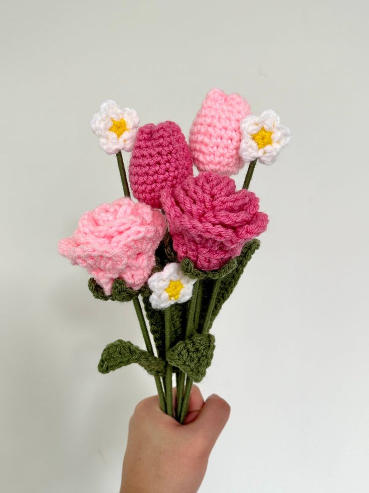 a hand holding a crocheted flower bouquet in pink, white and yellow colors